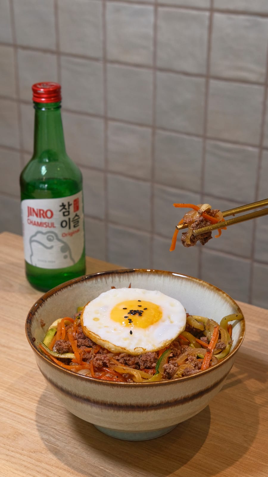 Bibimbap de bulgogi con huevo frito y verduras, con una botella de soju